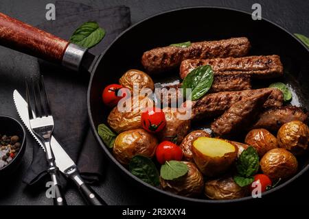Deliziose salsicce alla griglia e patate in una padella sfrigolante. Primo piano Foto Stock