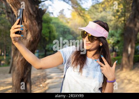 Giovane ragazza indiana da viaggio che indossa occhiali da sole e berretto scattando foto al selfie con lo smartphone Foto Stock