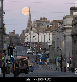 Guardando verso il West End di Union Street nel centro di Aberdeen come la Luna piena (rosa) si trova dietro Gilcomston Church spire poco prima dell'alba Foto Stock