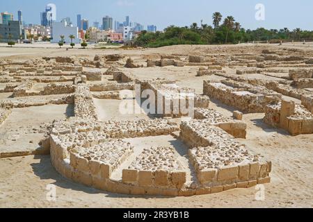 Rovine del forte Bahrain o Qall'at al-Bahrain con Manama moderno paesaggio urbano sullo sfondo, Bahrain Foto Stock