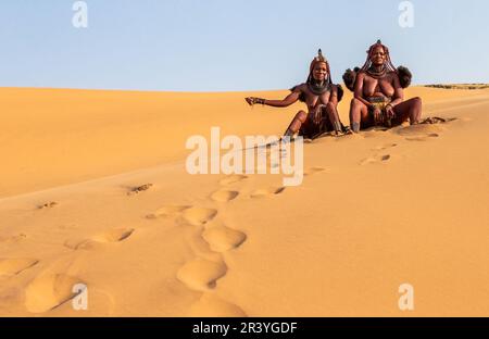 Due donne Himba sono sedute sulla sabbia nel deserto. Foto Stock