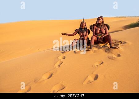 Due donne Himba sono sedute sulla sabbia nel deserto. Foto Stock