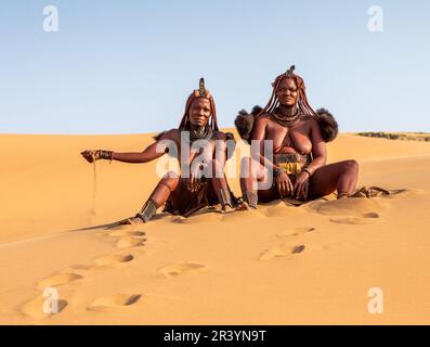 Due donne Himba sono sedute sulla sabbia nel deserto. Foto Stock