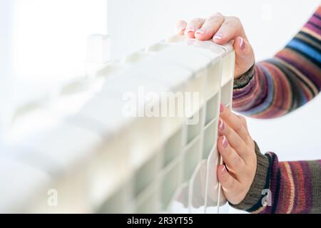 Donna che tocca il radiatore caldo con entrambe le mani Foto Stock