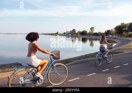 Adolescenti di diverse nazionalità e aspetto in bicicletta percorrono una strada cittadina. Le ragazze giovani e positive sorridono insieme Foto Stock