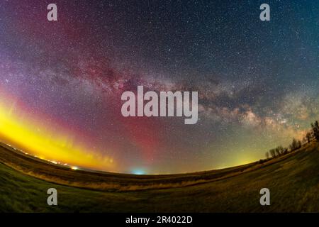 Un arco aurorale a sinistra attraverso l'orizzonte settentrionale con l'estate Via Lattea che sale, Alberta, Canaa. Foto Stock