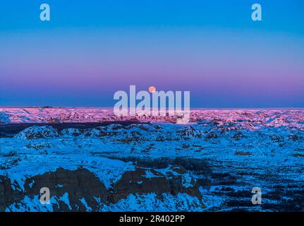 Luna piena che si innalza sopra i terreni innevati del Dinosaur Provincial Park, Alberta, Canada. Foto Stock