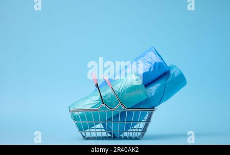 Rotoli di sacchetti di plastica in un cestino della spesa in miniatura su uno sfondo blu Foto Stock