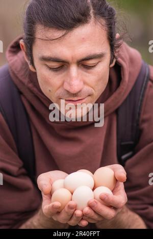 Felice giovane uomo Ritratto contadino tenendo le mani uova fresco Pollo biologico RawClose up galline ecologicamente coltivate in fienile di campagna agricola Foto Stock