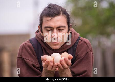 Felice giovane uomo Ritratto contadino tenendo le mani uova fresco Pollo biologico RawClose up galline ecologicamente coltivate in fienile di campagna agricola Foto Stock