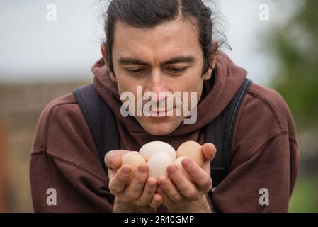 Felice giovane uomo Ritratto contadino tenendo le mani uova fresco Pollo biologico RawClose up galline ecologicamente coltivate in fienile di campagna agricola Foto Stock