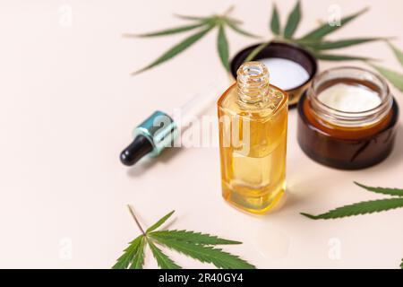 PRODOTTI di bellezza biologici PER IL CENTRO BENESSERE. Concetto di Medicina alternativa alle erbe. Crema cosmetica di cannabis, siero facciale e foglie di canapa su beige Foto Stock