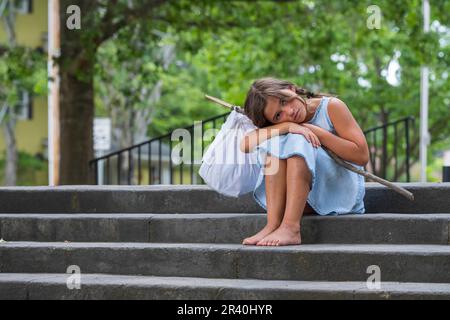 Un bambino scappato abbandonato affamato cerca cibo e riparo in un ambiente all'aperto Foto Stock