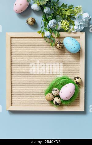 Concetto di accoglienza primaverile. Tavola da lettere, uova di Pasqua e fiori primaverili su sfondo blu pastello, compositi in stile minimalistico Foto Stock