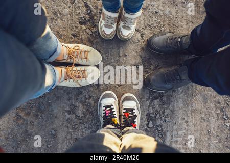 Quattro coppie di piedi di famiglia in piedi insieme sulla strada di terra. Selfie di quattro coppie gambe donna, bambino, uomo e tenager. Foto Stock