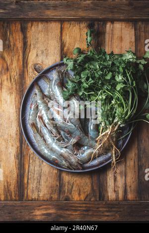 Pesce crudo. Gamberetti freschi con coriandolo su piatto grigio. Retro in legno. Foto Stock