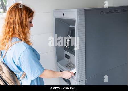 Donna dai capelli rossi che utilizza un ATM con accesso nfs senza contatto. Foto Stock