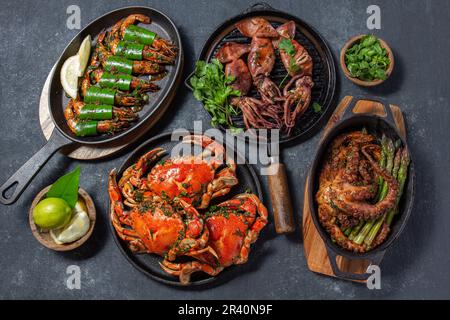 Set di piatti di pesce. Granchi, polpi, calamari e gamberetti sulle teglie e piatti di ghisa su fondo nero. Vista dall'alto. Foto Stock