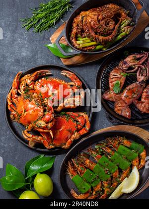 Set di piatti di pesce. Granchi, polpi, calamari e gamberetti sulle teglie e piatti di ghisa su fondo nero. Vista dall'alto. Foto Stock