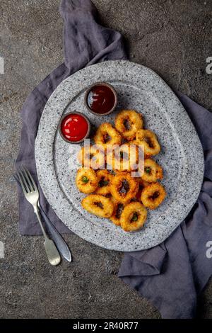 Calamari fritti anelli in pietra grigia piastra con salse. Grigio sfondo concreto Foto Stock