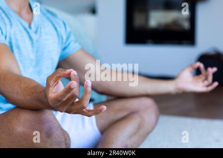 Sezione centrale dell'uomo biraciale seduto sul pavimento in camera da letto, meditando Foto Stock