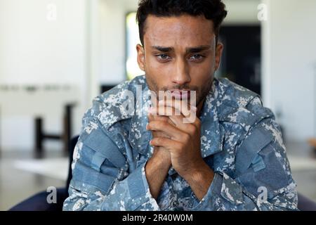 Preoccupato soldato biraciale maschio indossando uniforme militare, seduto in poltrona nel soggiorno di casa Foto Stock