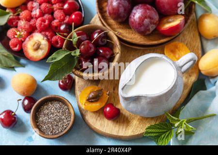 Ingredienti per un frullato sano. Latte e frutti di bosco (lampone, ciliegia, prugna, albicocca) su un piano di pietra. Mangiare sano, crudo Foto Stock