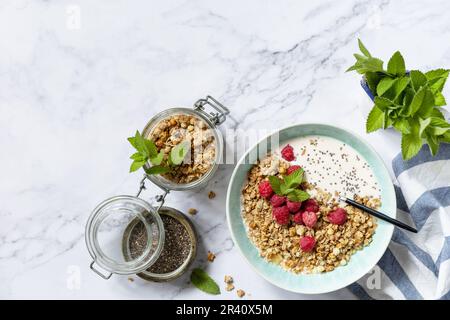 Colazione, dolce. Concetto di nutrizione di dieta. Granola fatta in casa con yogurt, semi di chia e lampone su un tavolo in marmo. V Foto Stock