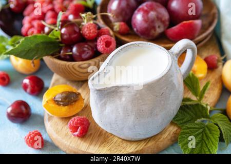 Ingredienti per un frullato sano. Latte e frutti di bosco (lampone, ciliegia, prugna, albicocca) su un piano di pietra. Mangiare sano, crudo Foto Stock