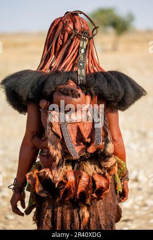 Figlio della tribù Himba dietro la madre. Foto Stock