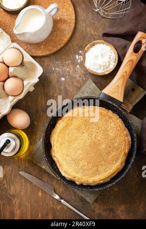 Festeggiamo la giornata delle fritture, cucinando una sana colazione. Deliziose crepes o frittelle fatte in casa in una padella e ingredienti su un r Foto Stock