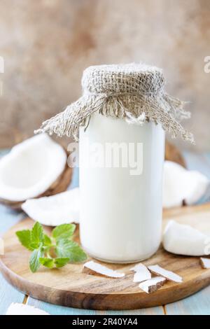 Latte alternativo vegano non caseario, contenuto sanitario. Latte di cocco biologico in una bottiglia su un tavolo rustico. Foto Stock