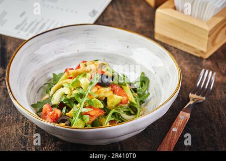 Insalata con calamari, rucola, sedano e avocado, pomodori e olive su piatto bianco su tavolo di legno Foto Stock