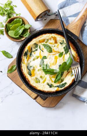 Spinaci e omelette al formaggio. Frittata di uova, paprika e spinaci in padella su un piano di marmo. Vista dall'alto. Foto Stock