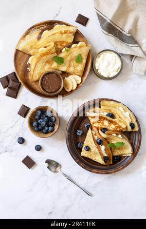 Festeggiamo il giorno delle Pancake, colazione sana. Deliziose crepes fatte in casa con caramello al cioccolato, banane e mirtilli e ricott Foto Stock