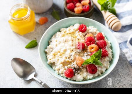 Porridge di farina d'avena in ciotola di ceramica decorata con lamponi di frutti di bosco freschi e semi di chia serviti con miele. Colazione sana e dietetica Foto Stock