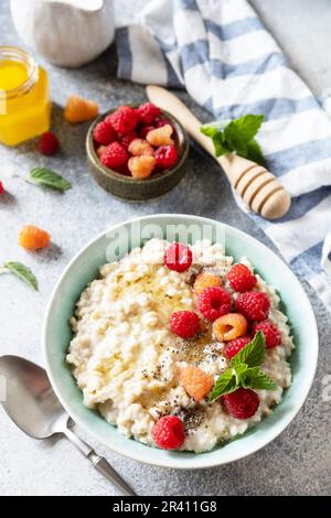 Porridge di farina d'avena in ciotola di ceramica decorata con lamponi di frutti di bosco freschi e semi di chia serviti con miele. Colazione sana e dietetica Foto Stock