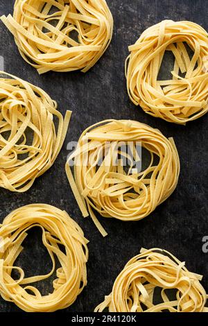 Tagliatelle nidi di pasta disposti su uno sfondo scuro: Diversi nidi di pasta secca di spaghetti posti su un piano cucina Foto Stock
