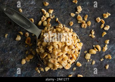 Nocciole tostate in una tazza di misurazione in acciaio inossidabile: Vista laterale ravvicinata dei ciottoli tagliati impilati in una paletta di metallo Foto Stock