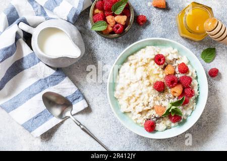 Porridge di farina d'avena in ciotola di ceramica decorata con lamponi di frutti di bosco freschi e semi di chia serviti con miele. Colazione sana e dietetica Foto Stock