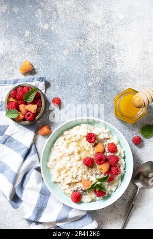 Porridge di farina d'avena in ciotola di ceramica decorata con lamponi di frutti di bosco freschi e semi di chia serviti con miele. Colazione sana e dietetica Foto Stock