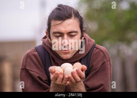 Felice giovane uomo Ritratto contadino tenendo le mani uova fresco Pollo biologico RawClose up galline ecologicamente coltivate in fienile di campagna agricola Foto Stock