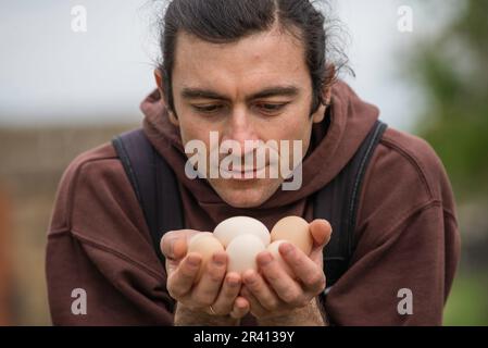 Felice giovane uomo Ritratto contadino tenendo le mani uova fresco Pollo biologico RawClose up galline ecologicamente coltivate in fienile di campagna agricola Foto Stock