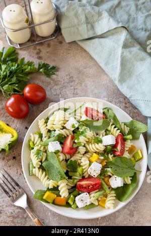 Cibo italiano - insalata con pasta senza glutine, spinaci, pomodori, fagioli e formaggio feta su un tavolo di pietra. Cibo sano, vegetariano Foto Stock