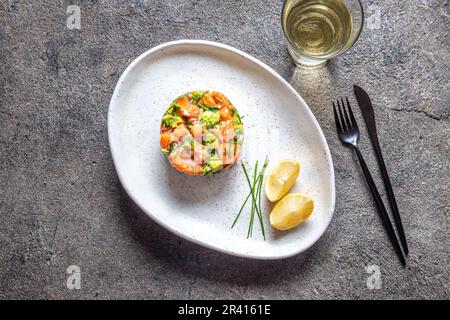 La cucina peruviana. Ceviche di salmone con avocado, cipolline e succo di limone sulla piastra bianca servita con vino bianco Foto Stock