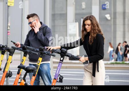 Ragazza in piedi su una strada con scooter elettrico nel parcheggio. Trasporti e viaggi in città Foto Stock