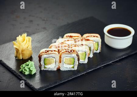 Sushi roll con anguilla, avocado, formaggio cremoso su sfondo scuro. Menu sushi. Cucina giapponese. Foto Stock