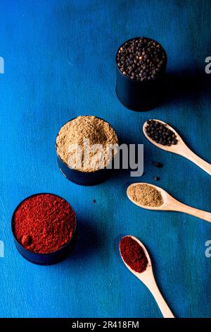 Lattine di latta e cucchiai di legno, ripieni di spezie su fondo blu dipinto a mano. Con spazio di copia Foto Stock