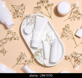 Tubi di plastica bianca, vasi, e rami di gypsofila su uno sfondo beige, contenitori per creme cosmetiche e gel, pubblicità a. Foto Stock