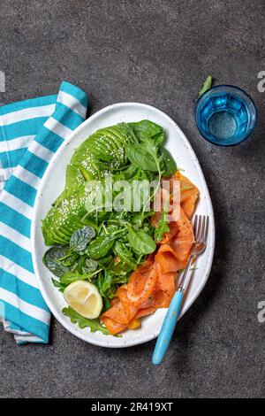 Bassa di un glucide insalata. Gli spinaci, rucola con insalata di avocado e salmone. Nero lo sfondo di calcestruzzo, piastra bianca, vista dall'alto Foto Stock